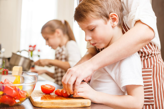 Small boy cutting in slices vegetables with mother