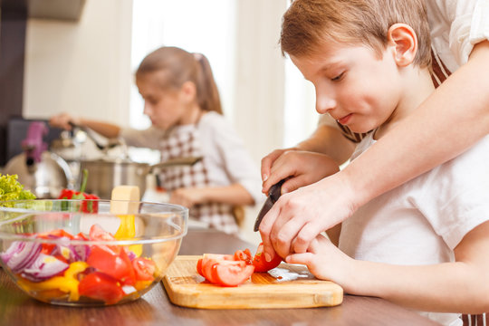 Small boy cutting in slices vegetables with mother