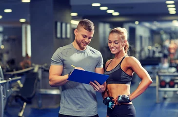 Foto op Canvas smiling young woman with personal trainer in gym © Syda Productions