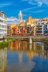 Church of Sant Feliu, colorful yellow and orange houses and bridge Pont de Sant Agusti reflected in water river Onyar, in Girona, Catalonia, Spain