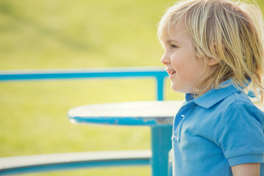 Happy Smiling Blond Child Play With Carousel In A Park