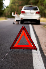 Red warning triangle and broken car in the middle of forrest