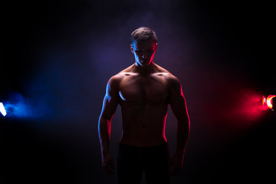 Handsome Power Athletic Man Bodybuilder. Fitness Muscular Body On Dark Colour Smoke Background. Perfect Male. Awesome Bodybuilder Silhouette., Tattoo, Posing. 