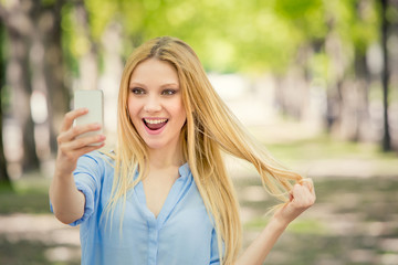 smiling blonde young woman with phone portrait in a green cityscape