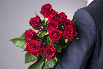 Fototapeta premium Man with bouquet of red roses on a gray background
