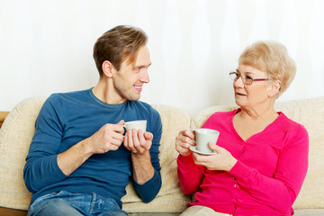 Mother and son sitting on couch and drinking tea or coffee
