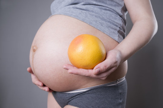 Pregnancy and nutrition - pregnant woman with grapefruit in hand on gray background
