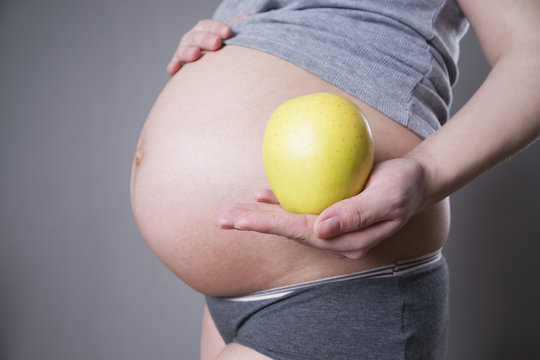 Pregnancy and nutrition - pregnant woman with apple in hand on gray background