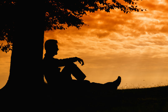 Man silhouette sitting under tree on cloudy day outdoor