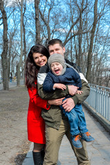 Fototapeta na wymiar Portrait of happy young family spending time together in green nature in park. Mother, father and son having fun outdoors on a spring sunny day. Concept of happy family life, love and happiness. 