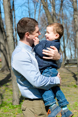 Father and son having fun outdoors on a spring sunny day. Happy smiling little boy in the arms of his dad. Concept of happy family life, love and happiness. 