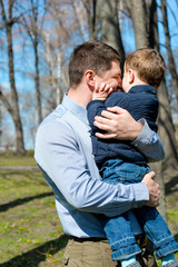 Father and son having fun outdoors on a spring sunny day. Happy smiling little boy in the arms of his dad. Concept of happy family life, love and happiness. 