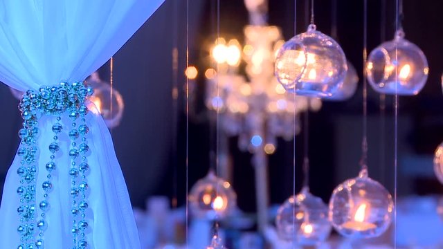 Hanging lighting candles. Hung 6 flamed candles with candlestick at the background. White blind with silver chain The interior of the hall pn in the party , celebration.