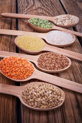 Groats in spoons on wooden table