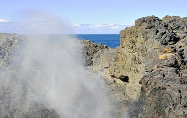     Water spraying out in force from the Kiama Blowhole surrounded by volcanic cliffs

