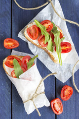 Bruschetta with cotage cheese, tomatoes and arugula on blue wooden background