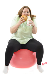 Corpulent woman having addiction to unhealthy food, eating high calories food sitting on fitness ball