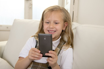  female child with blond hair sitting on couch using internet app on mobile phone