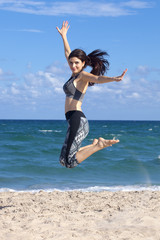 Pretty woman jumping with excitement on a beach with ocean in the background