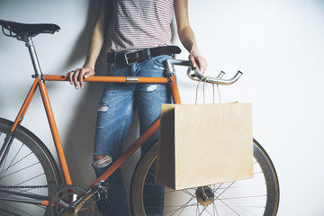 Closeup of woman wearing blue jeans and standing with vintage orange bike and blank paper package with handles