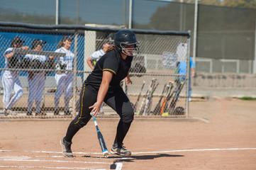 Strong softball player in black uniform dropping the bat while running to first. 