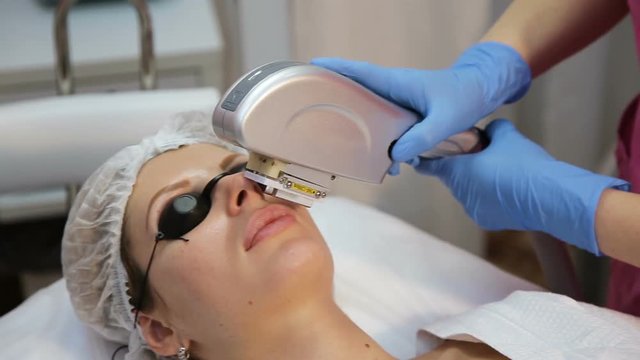Woman with closed eyes getting photo rejuvenation procedure in a beauty salon.Cosmetician perfiming photo rejuvenation cosmetology procedure for a woman.Skin care. Young woman receiving facial beauty