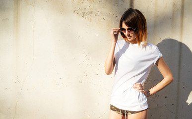 Shapely young girl wearing in a white blank t-shirt and sunglasses posing against a background of a...