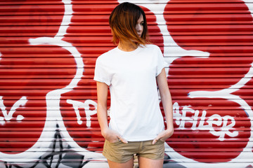 young attractive girl wearing a white t-shirt standing on a graffiti wall background - obrazy, fototapety, plakaty