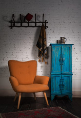 Composition of vintage orange armchair, blue cupboard, wall hanger with ornate scarf and red fez in studio