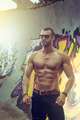 Fototapeta na wymiar Young fit macho man posing in front of graffiti wall
