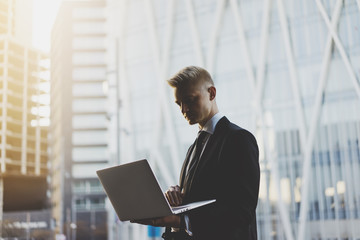 Young professional businessman using laptop outside while working on new project of modern office or living house, flare light