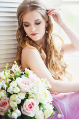 Portrait of pretty young girl in a sweet dress and long blonde hair sitting on a window with flowers composition