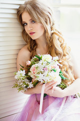 Portrait of pretty young girl in a sweet dress and long blonde hair sitting on a window with flowers composition
