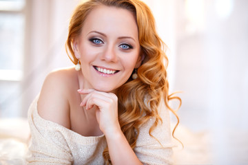 Naklejka premium Young beautiful woman in a warm pullover in a light bedroom in a morning. Close up portrait, blue eyes and natural makeup