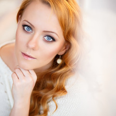 Young beautiful woman in a warm pullover in a light bedroom in a morning. Close up portrait, blue eyes and natural makeup