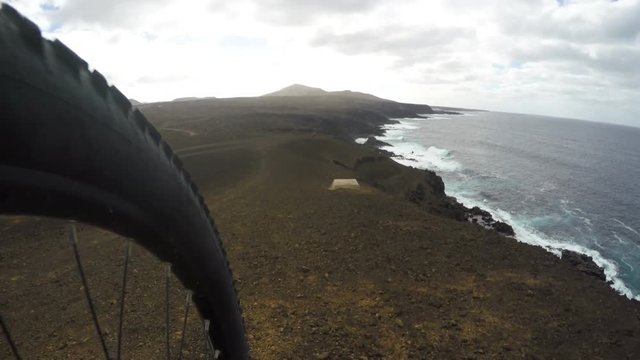 Mountain bike wheel and tire close up biking downhill on cliff. Bicycle moving on mountain by sea. Offroad bike is in motion against cloudy sky. It is in speed on mount surrounded by water. ACTION CAM