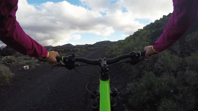 Female cyclist riding mountain bike POV. Young woman cyclist riding bicycle on mountain. Dedicated woman in sportswear is cycling in nature. She is living her healthy lifestyle. Shaky ACTION CAMERA