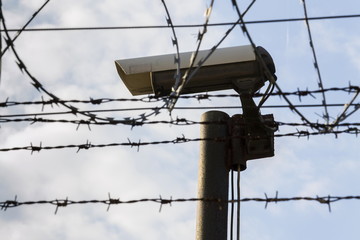 Obraz premium Security camera behind barbed wire fence stretched around prison walls