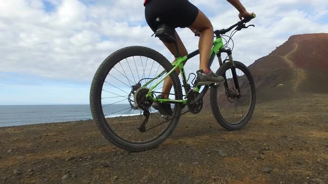 Woman cycling riding bicycle on mountain by sea on mountain bike. Sporty woman cyclist biking in nature. Active fitness girl living healthy lifestyle. ACTION CAMERA, Lanzarote, Canary Islands, Spain.