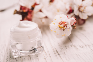 Natural facial cream with spring blossom on rustic wooden background