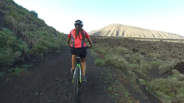Mountain biking woman cycling on MTB riding on bike trail. Determined cyclist in sportswear is cycling.  Smiling female is living healthy lifestyle. Lanzarote, Canary Islands, Spain. ACTION CAMERA.