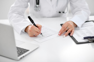 Close-up of a female doctor filling  out application form , sitting at the table in the hospital