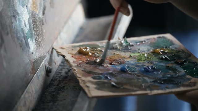 the artist puts brush to the palette of paints on an easel