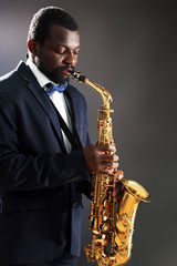 African American jazz musician playing the saxophone on grey background