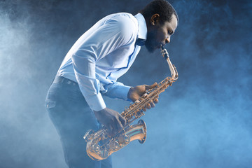 African American jazz musician playing the saxophone against colorful smoky background - obrazy, fototapety, plakaty