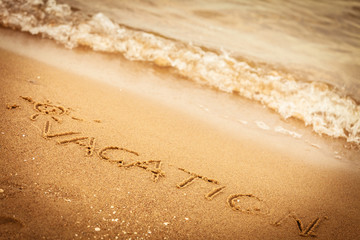 The word vacation written in the sand on a beach