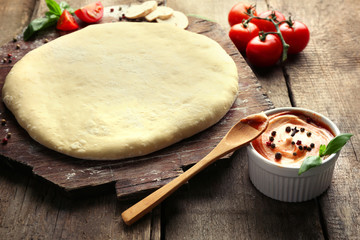 Fresh dough prepared for pizza with tomatoes and sliced mushrooms on a wooden board, close up