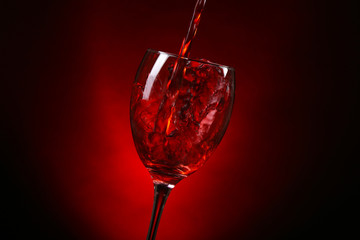 Wine pouring in glass on dark red background