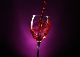 Wine pouring in glass on dark purple background