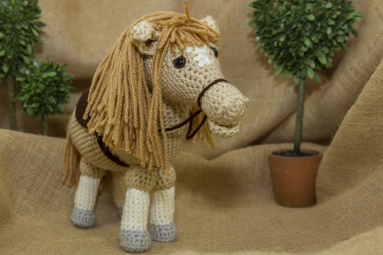 A handcrafted crochet toy horse photographed on a rustic burlap backdrop.